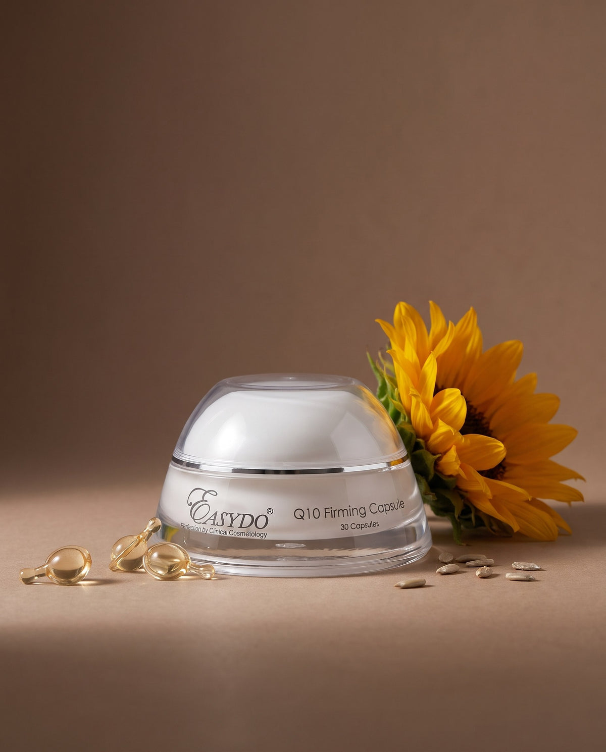 A clear cosmetic jar with a white lid and black text reading 'Easydo Q10 Firming Cream' on a warm brown studio background, styled with a yellow sunflower and scattered golden capsules.
