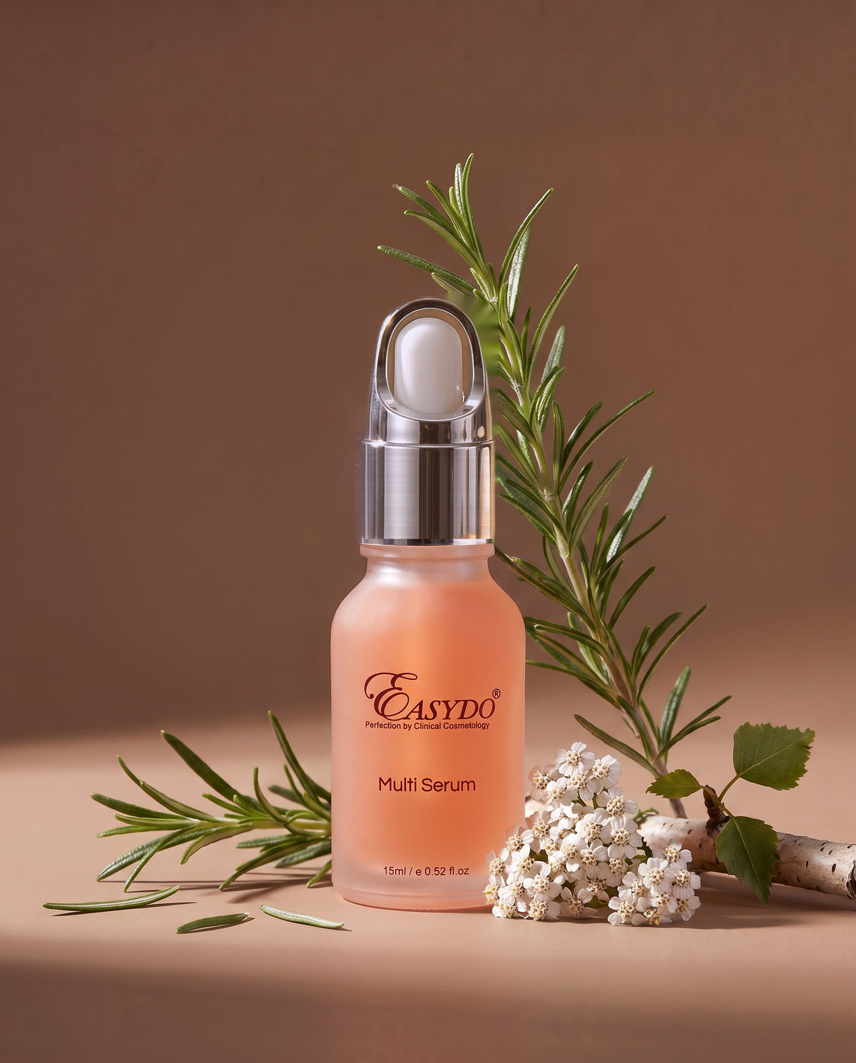 A bottle of Easydo Multi Serum with a peach-colored liquid and silver dropper cap, styled with rosemary and white flowers on a warm brown background.